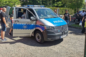 Na zdjęciu widać policyjny radiowóz, w którym siedzi dziewczynka trzymająca w dłoni watę cukrową.