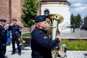 Na zdjęciu widać policjanta trzymającego w dłoniach dużą trąbę do grania.