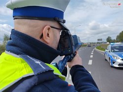 Zdjęcie policjanta trzymającego urządzenie do pomiaru prędkości.