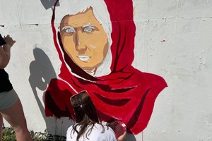 Na zdjęciu widać jak uczennice malują na murze postać kobiety w czerwonej chuście.