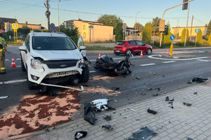 Na miejscu widać miejsce zderzenia się białego samochodu z motocyklem. Motocykl leży na jezdni.