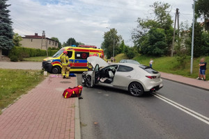 Na zdjęciu widać uszkodzony srebrny samochód, a za nim stojącą karetkę pogotowia.