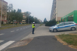 Na zdjęciu widać policjanta i radiowóz prowadzącego działania w rejonie przejścia dla pieszych.