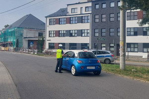 Na zdjęciu widać policjanta podczas kontroli, stojącego przy niebieskim samochodzie.