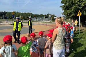 Na zdjęciu widać policjantów, wychowawców i przedszkolaków na terenie miasteczka ruchu drogowego. Policjanci ubrani są w odblaskowe kamizelki.