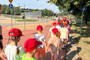 Na zdjęciu widać przedszkolaków na terenie miasteczka ruchu drogowego. Dzieci przemieszczają się w parach.