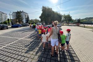 Na zdjęciu widać policjantów, wychowawców i przedszkolaków, które stoją w kolejce do radiowozu.