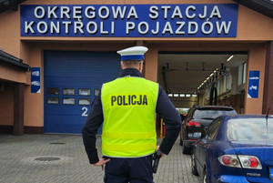 Na zdjęciu widać policjanta i samochody, a w tle budynek stacji diagnostycznej,