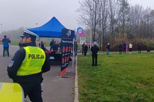 Na zdjęciu widać policjanta ubranego w odblaskową kamizelkę a w tle trasę biegu w Parku Cegielnia.