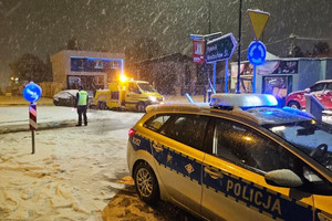 Na zdjęciu widać radiowóz, policjanta, a w tle lawetę i ciemny samochód.