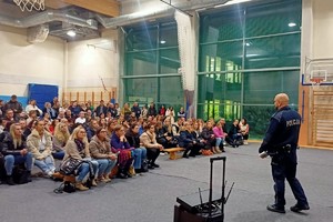 Na zdjęciu widać policjanta oraz uczestników spotkania w sali gimnastycznej.