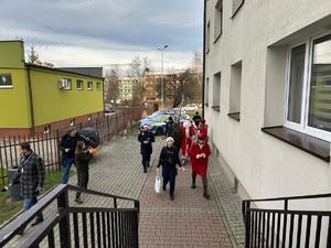 Na zdjęciu widać policjantów oraz osoby przebrane w kolorowe stroje, zmierzających do wejścia do budynku.