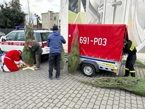 Na zdjęciu widać samochód straży pożarnej z przyczepką, z której wyciągane są choinki.