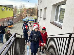 Na zdjęciu widać policjantów oraz osoby przebrane w kolorowe stroje, a w tle sąsiedztwo bloku mieszkalnego.