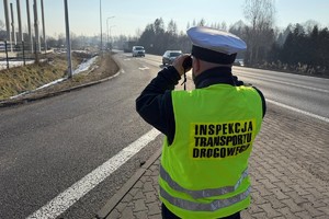 Na zdjęciu widać inspektora transportu drogowego obserwującego drogę przy pomocy lornetki.