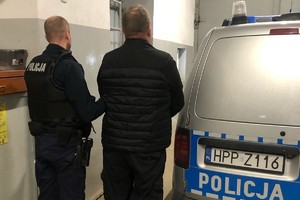 Na zdjęciu widać policjanta, radiowóz oraz zatrzymanego.
