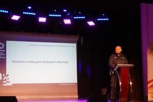 Na zdjęciu widać policjanta przemawiającego na scenie.