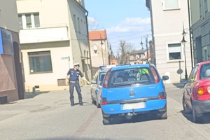 Na zdjęciu widać niebieski samochód oraz policjanta stojącego koło niego.