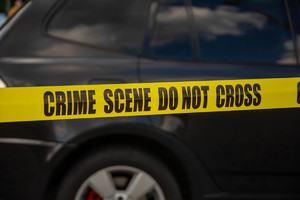 Zdjęcie przedstawia żółtą taśmę z napisem &quot;crime scene do not cross&quot;. W tle czarny pojazd.