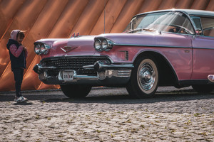 Na zdjęciu widać różowego, starego cadillac&#039;a. Po lewej stronie stoi dziewczynka podziwiająca samochód. W tle muzeum ognia.