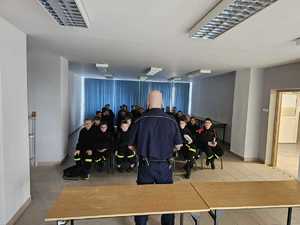 Na zdjęciu widać policjanta w sali odpraw oraz uczestników spotkania.