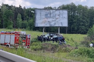Na zdjęciu widać miejsce zdarzenia drogowego, bilboard i uszkodzony samochód.