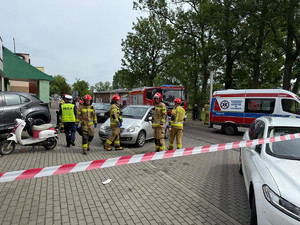 Na zdjęciu widać miejsce zdarzenia drogowego, zaparkowane samochody, policjantów i strażaków.