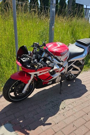 Na zdjęciu widać biały uszkodzony samochód dostawczy oraz czerwony uszkodzony motocykl.