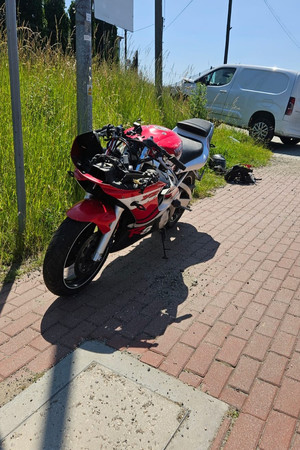 Na zdjęciu widać czerwony uszkodzony motocykl, a w tle biały uszkodzony samochód dostawczy.