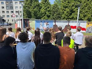 Na zdjęciu widać galerię murali podczas ich tworzenia, a także uczniów i zgromadzonych podczas akcji pod nazwą &quot;Plenerowa lekcja patriotyzmu&quot;.