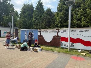 Na zdjęciu widać galerię murali podczas ich tworzenia, a także uczniów i zgromadzonych podczas akcji pod nazwą &quot;Plenerowa lekcja patriotyzmu&quot;.