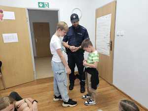 Na zdjęciu widać policjanta oraz uczestników półkolonii podczas wspólnych zajęć.