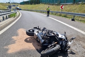 Na zdjęciu widać uszkodzony motocykl, radiowóz, policjanta oraz śmigłowiec LPR, w tle widać fragment autostrady.