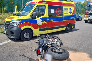 Na zdjęciu widać uszkodzony motocykl, radiowóz, policjanta oraz śmigłowiec LPR, w tle widać fragment autostrady.