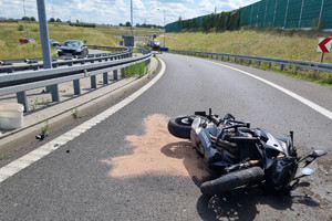 Na zdjęciu widać uszkodzony motocykl, radiowóz, policjanta oraz śmigłowiec LPR, w tle widać fragment autostrady.