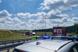 Na zdjęciu widać uszkodzony motocykl, radiowóz, policjanta oraz śmigłowiec LPR, w tle widać fragment autostrady.