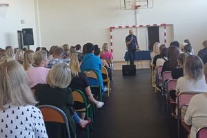 Na zdjęciu widać rodziców uczniów zgromadzonych w sali oraz policjanta i przedstawiciela szkoły.
