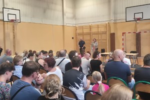 Na zdjęciu widać rodziców uczniów zgromadzonych w sali oraz policjanta i przedstawiciela szkoły.