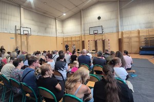 Na zdjęciu widać rodziców uczniów zgromadzonych w sali oraz policjanta i przedstawiciela szkoły.