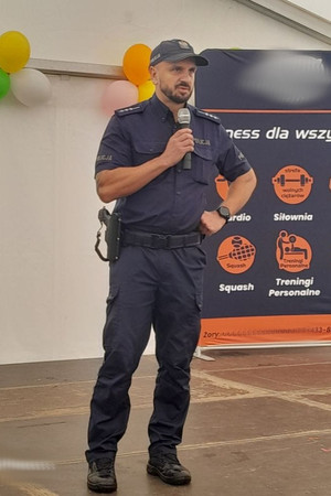Na zdjęciu widać policjanta z mikrofonem na scenie.