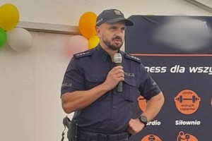 Na zdjęciu widać policjanta z mikrofonem na scenie.