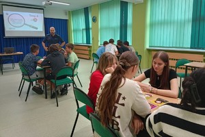 Na zdjęciu widać policjanta w sali lekcyjnej oraz uczniów siedzących w ławkach.