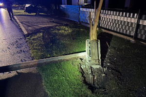 Na zdjęciu widać miejsce zdarzenia drogowego. Powalony słup, a w tle zabudowania.