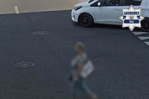 Na zdjęciu widać przysklepowy parking oraz postać, która jest rozmazana.