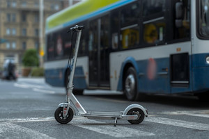 Grafika przedstawia hulajnogę a w tle autobus.