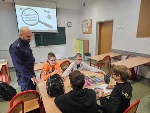 Na zdjęciu widać policjanta oraz uczniów w sali lekcyjnej podczas przeprowadzanych zajęć.