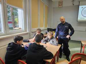 Na zdjęciu widać policjanta oraz uczniów w sali lekcyjnej podczas przeprowadzanych zajęć.