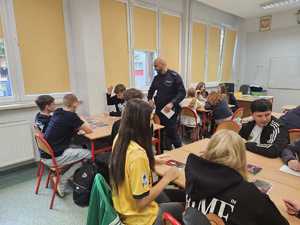 Na zdjęciu widać policjanta oraz uczniów w sali lekcyjnej podczas przeprowadzanych zajęć.