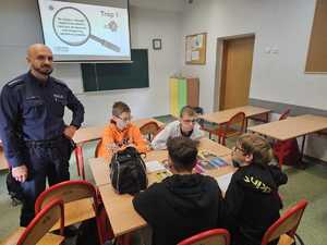 Na zdjęciu widać policjanta oraz uczniów w sali lekcyjnej podczas przeprowadzanych zajęć.