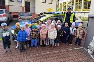 Na zdjęciu widać policjanta, radiowóz oraz przedszkolaków.